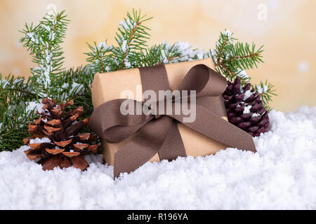Weihnachtsgeschenk in braunes Papier und Farbband mit Tannenzapfen und immergrünen Baum auf einem schneebedeckten Oberfläche und hellen Hintergrund gewickelt Stockfoto