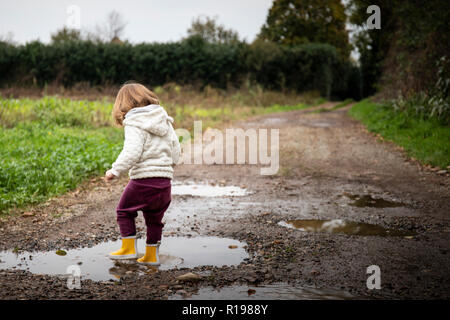 Kleinkind Mädchen, Rückansicht, Planschen in Pfützen in schlammigen Weg mit gelber regen Stiefel. Kopieren Sie Speicherplatz frei ist. Stockfoto