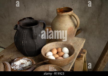 Zwei frühe mittelalterliche Krüge und eine hölzerne Schüssel voller Eier. Stockfoto