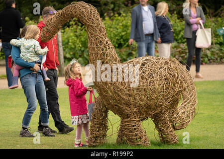 Junges Mädchen, das auf einem handgefertigten Willow Woven Dinosaurier, RHS Garden, Harlow Carr, Harrogate, North Yorkshire, England. Stockfoto