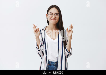 Kreuzung meine Finger zu schreien für Lieblings Fußballmannschaft. Portrait von stilvollen gut aussehende Freundin in modischen Brille und Bluse, schürzte die Lippen und frow Stockfoto