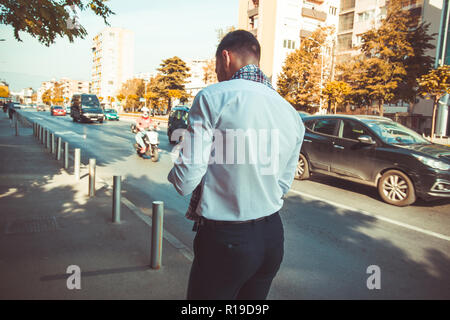 Eine moderne Geschäftsmann ist zu Fuß auf den Bürgersteig auf der gegenüberliegenden Straßenseite gibt es einen riesigen Stau Stockfoto