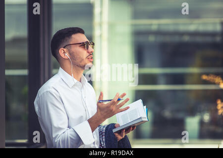 Moderne kaukasischen Mann mit Notizbuch und Stift während der Wiedergabe von Musik Stockfoto