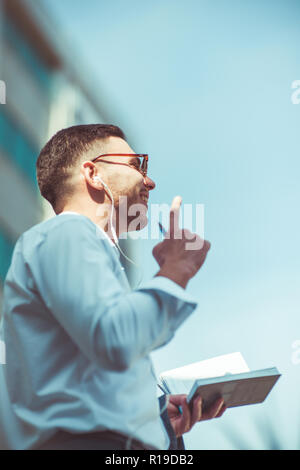 Moderne kaukasischen Mann mit Notizbuch und Stift während der Wiedergabe von Musik Stockfoto