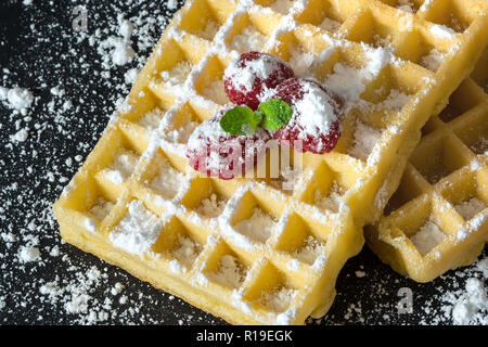 Sweet Toast, Waffeln mit Himbeeren und einem Zweig Minze und Zucker Pulver Nahaufnahme Makro auf schwarzem Hintergrund Stockfoto