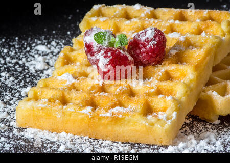 Sweet Toast, Waffeln mit Himbeeren und einem Zweig Minze und Zucker Pulver Nahaufnahme Makro auf schwarzem Hintergrund Stockfoto