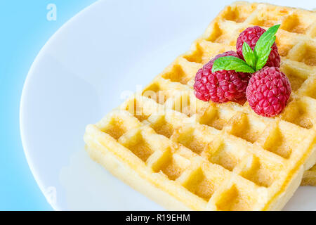 Sweet Toast, Waffeln mit Himbeeren und einem Zweig Minze oben auf einem weißen Teller Nahaufnahme Makro auf einem blauen Hintergrund Stockfoto