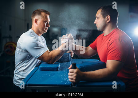 Zwei Arm Ringer kämpfen auf Ihren Händen am Tisch mit Stiften, der den Staub aus dem talkum in der Luft, wrestling Wettbewerb. Ringen Herausforderung, Power s Stockfoto