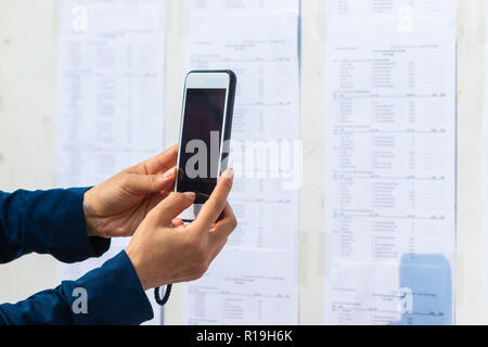 Frau unter Bild Der ausgehängte Zeitplan auf einem im Bulletin Board mit Ihrem smart phone Kamera Stockfoto