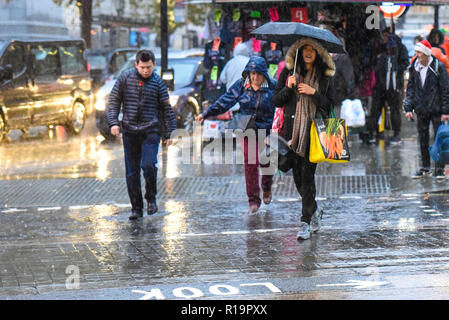 Touristen genossen sonnigen warmen Wetter während der Tag in London, aber das hat zu heavy rain geändert. Die Leute laufen durch Wasser mit Schirm Stockfoto