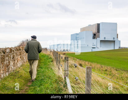 Torness, East Lothian, Schottland, Vereinigtes Königreich, 10. November 2018. UK Wetter: Trotz der Sturm an der West Küste der UK, Eastern Scotland ist mild mit nur einer leichten Brise. Ein älterer Mann Spaziergänge entlang der Küste neben dem Kernkraftwerk Torneß Stockfoto