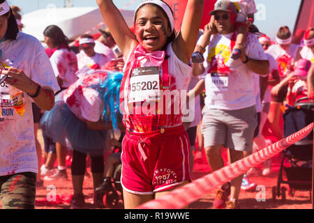 Kleines Mädchen von gemischten Rennen oder farbige Ethnie ca. 8-10 Jahre alt springen auf und ab, die Arme in der Luft in roter Farbe pulverbeschichtet, während ein Sommer Colour run Veranstaltung angehoben Stockfoto