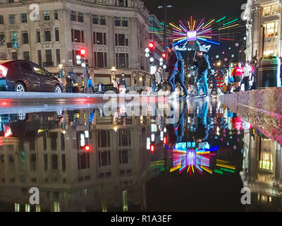Lodnon, UK. 10 Nov, 2018. Reflexion der Oxford Street Weihnachtsbeleuchtung und Dekoration in eine Pfütze von Wasser nach starken Regenfällen in London. Credit: SOPA Images Limited/Alamy leben Nachrichten Stockfoto