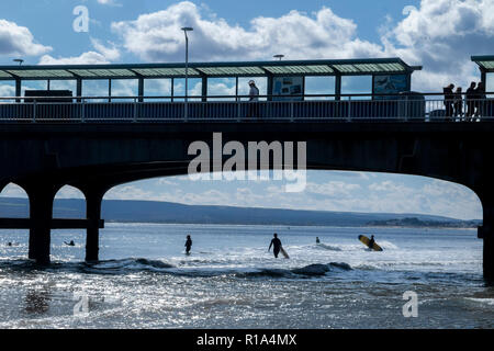 Surfer im Meer am Strand von Bournemouth im Hochsommer, unterhalb der berühmten Pier Stockfoto