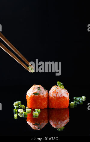 Appetitlich gebackene Sushi Roll mit Fisch, grüne Zwiebeln mit Stäbchen auf einem schwarzen Hintergrund mit Reflexion Menü und Restaurant Konzept Stockfoto
