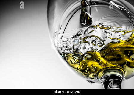 Strom des weißen Wein in ein Glas gießen, Weißwein splash Close-up auf grauem Hintergrund. Schwarz-weiß Foto mit Farbe des Weines. Stockfoto