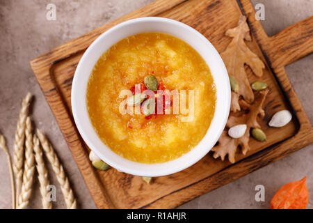 Kürbis Suppe pürieren, in eine keramische Schüssel mit Kürbiskernen und würzig chili Pfeffer würzen. Blick von oben. Stockfoto