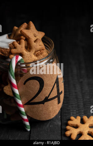 Papier Variable mit der Nummer 24 auf ein Glas Glas voll mit hausgemachter Lebkuchen Kekse und eine rot-grüne abgestreift Candy Cane Stockfoto