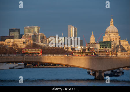 Skyline von London bei Sonnenuntergang von der Themse. Menschen und Busse Kreuzung Waterloo Bridge als Gebäude der Stadt sind beleuchtet durch die letzten Strahlen der Sonne. Stockfoto