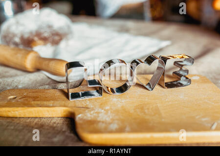 Backformen auf einem Holzbrett mit gebackenem Mehl. Gerollte Teig mit einem Muster und Cookie in verschiedenen Formen. Love Theme. Keks kochen backgrou Stockfoto