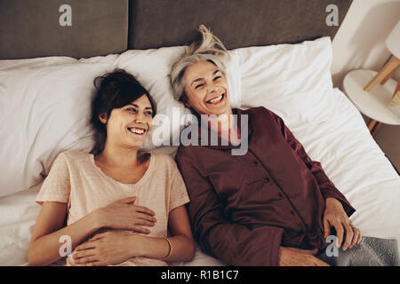 Mutter und Tochter lag auf dem Bett und lachte. Frau verbringen Zeit mit ihrer betagten Mutter liegend auf Bett zu Hause. Stockfoto