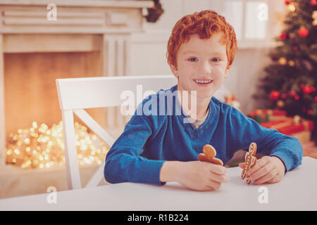 Angenehme Junge hält zwei Lebkuchen Männer und posieren Stockfoto