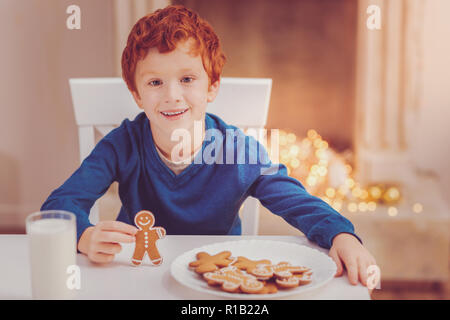 Angenehme Junge an den Tisch stellen und halten Gingerbread Man Stockfoto