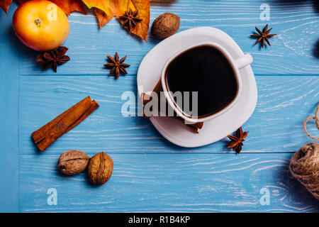 Schwarzer Kaffee in weisser Schale auf eine Untertasse mit Zimt Nussbaum Anis und Apple auf eine blaue Fläche Stockfoto