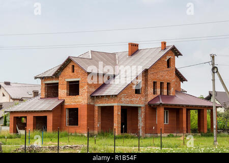 Großes, modernes zweistöckiges nicht New Brick Familie Ferienhaus Haus mit steilen braun Schindeldach, Garagen, hohe Schornsteine auf blauen Himmel Hintergrund. Nachteile Stockfoto