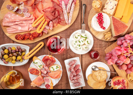 Charcuterie Verkostung. Viele verschiedene Wurst und Schinken, Aufschnitt, und eine Käseplatte, geschossen von oben auf eine rustikale Hintergrund mit Gläsern Wein Stockfoto