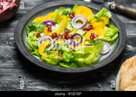 Gesunde Ernährung, frischer Salat mit lila Zwiebel und Granatapfel Samen auf dunklem Holz Hintergrund Stockfoto