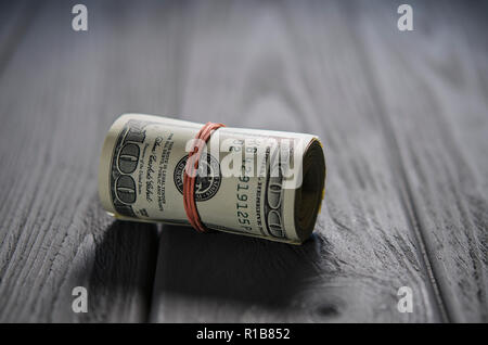 Eine dicke Rolle von hundert Dollar Banknoten gebunden einer Red Rubber Band liegt auf dem grauen Holz Tisch Stockfoto