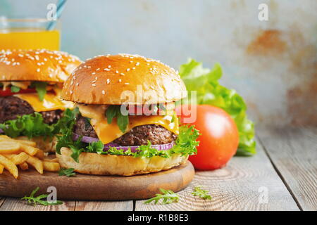 Zwei frische hausgemachte Burger mit Bratkartoffeln und Orangensaft auf einem Holztisch. Mit Platz kopieren Stockfoto