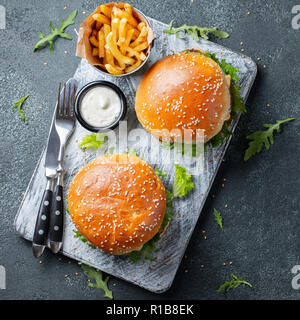 Lecker gegrilltes home Burger mit Rindfleisch, Tomaten, Käse, Gurken und Salat auf einem dunklen Stein Hintergrund. Ansicht von oben. Fast Food und Junk food Konzept Stockfoto