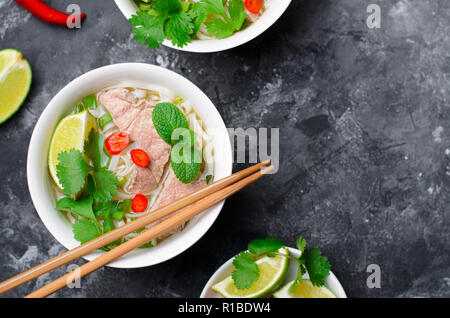 Traditionelle vietnamesische Suppe Pho Bo mit Reis Nudeln, Rindfleisch und Kräutern auf dunklem Hintergrund, asiatische Küche Stockfoto