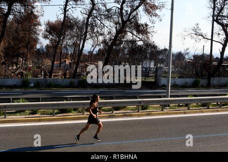 Athen, Griechenland. 11 Nov, 2018. Die Teilnehmer laufen hinter einem verbrannten Fläche von Mati Dorf, wo 99 Menschen bei einem Waldbrand im letzten Sommer gestorben, während der Athen Marathon 2018. (Bild: © aristidis VafeiadakisZUMA Draht) Stockfoto