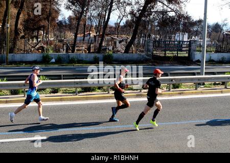 Athen, Griechenland. 11 Nov, 2018. Die Teilnehmer laufen hinter einem verbrannten Fläche von Mati Dorf, wo 99 Menschen bei einem Waldbrand im letzten Sommer gestorben, während der Athen Marathon 2018. (Bild: © aristidis VafeiadakisZUMA Draht) Stockfoto