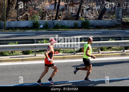 Athen, Griechenland. 11 Nov, 2018. Die Teilnehmer laufen hinter einem verbrannten Fläche von Mati Dorf, wo 99 Menschen bei einem Waldbrand im letzten Sommer gestorben, während der Athen Marathon 2018. (Bild: © aristidis VafeiadakisZUMA Draht) Stockfoto