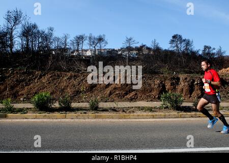 Athen, Griechenland. 11 Nov, 2018. Die Teilnehmer laufen hinter einem verbrannten Fläche von Mati Dorf, wo 99 Menschen bei einem Waldbrand im letzten Sommer gestorben, während der Athen Marathon 2018. (Bild: © aristidis VafeiadakisZUMA Draht) Stockfoto