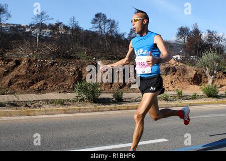 Athen, Griechenland. 11 Nov, 2018. Die Teilnehmer laufen hinter einem verbrannten Fläche von Mati Dorf, wo 99 Menschen bei einem Waldbrand im letzten Sommer gestorben, während der Athen Marathon 2018. (Bild: © aristidis VafeiadakisZUMA Draht) Stockfoto