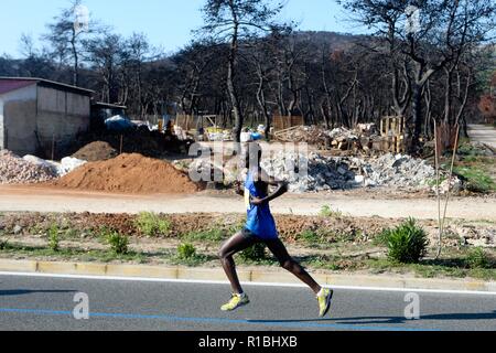 Athen, Griechenland. 11 Nov, 2018. Die Teilnehmer laufen hinter einem verbrannten Fläche von Mati Dorf, wo 99 Menschen bei einem Waldbrand im letzten Sommer gestorben, während der Athen Marathon 2018. (Bild: © aristidis VafeiadakisZUMA Draht) Stockfoto