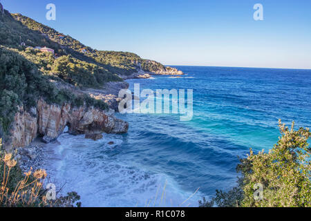 Blick auf das Meer mit Schaum Wellen, Felsen und Hügel bedeckt mit Wäldern. Häuser in den Wald. Griechenland Stockfoto