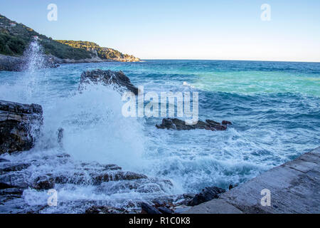 Blick auf das Meer und die Hügel von der Pier. Spritzer von Wasser aus dem Meer Wellen gegen die Felsen. Griechenland Stockfoto