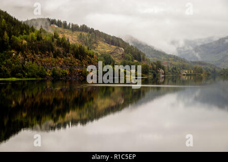 Schöne Reflexion im Tyrifjorden (Lake Tyri) nach einem regnerischen Tag in Norwegen. Dramatischer Himmel, Nebel, Bäume und Berge spiegeln sich perfekt in der Stockfoto