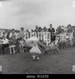 1967, historische, in einem englischen Dorf Sommer Fete, eine Mutter und ihre Tochter als "gekleidet wenig Bo-peep", eine Figur aus der beliebten Kinder Kinderlieder über eine Schäferin, laufen in einem Feld mit kleinen Schaf oder Lamm, England, UK. Stockfoto