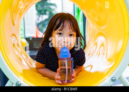 Lächelnd asiatischen Mädchen Trinkwasser in den Spielplatz. Stockfoto
