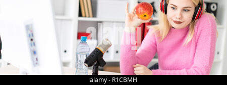 Ein junges Mädchen mit Kopfhörern am Tisch sitzen und mit einem Apfel. Stand vor ihr Mikrofon. Stockfoto