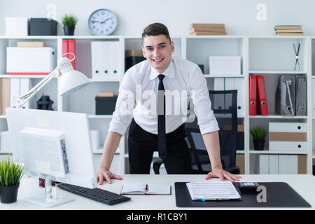 Ein junger Mann steht in den Büro- und legte seine Hände auf den Tisch. Stockfoto