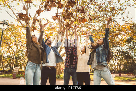 Eine Gruppe von Freunden im Park Spaß Blätter Werfen in die Luft Stockfoto