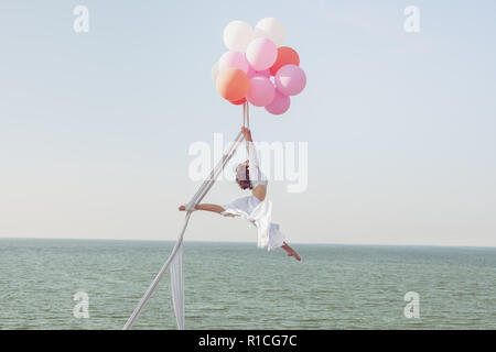 Junge Frau schwebt in der Luft auf Ballons über dem Meer. Stockfoto